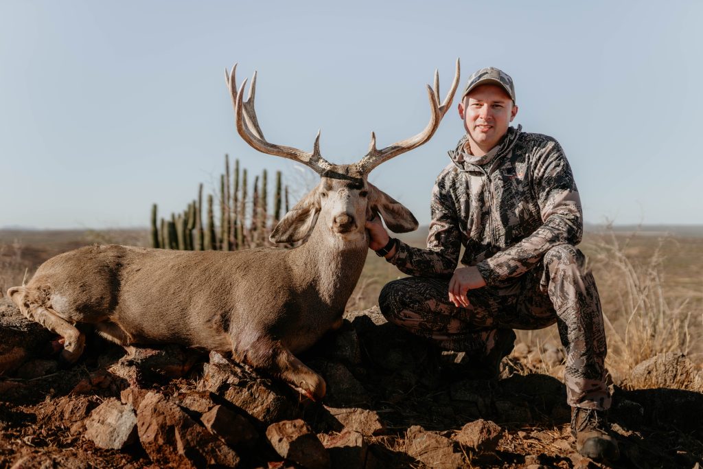 Hunter with trophy mule deer buck in Mexican desert landscape with saguaro cacti documented by Wildsmith international hunting videography