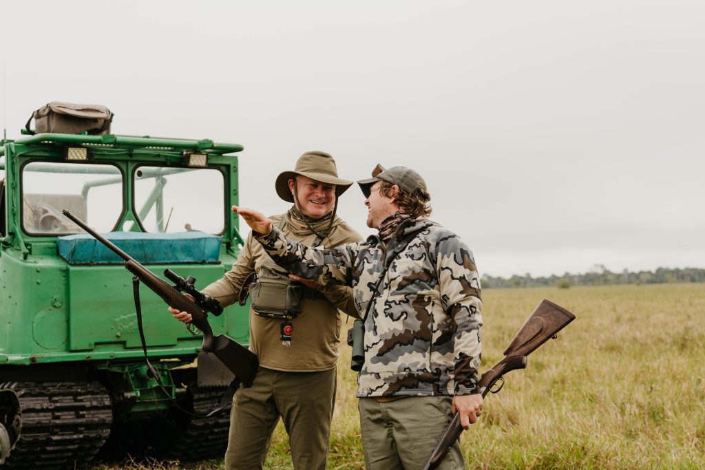 Professional hunting guide and client celebrating successful hunt beside vintage Land Rover in South African grasslands documented by Wildsmith